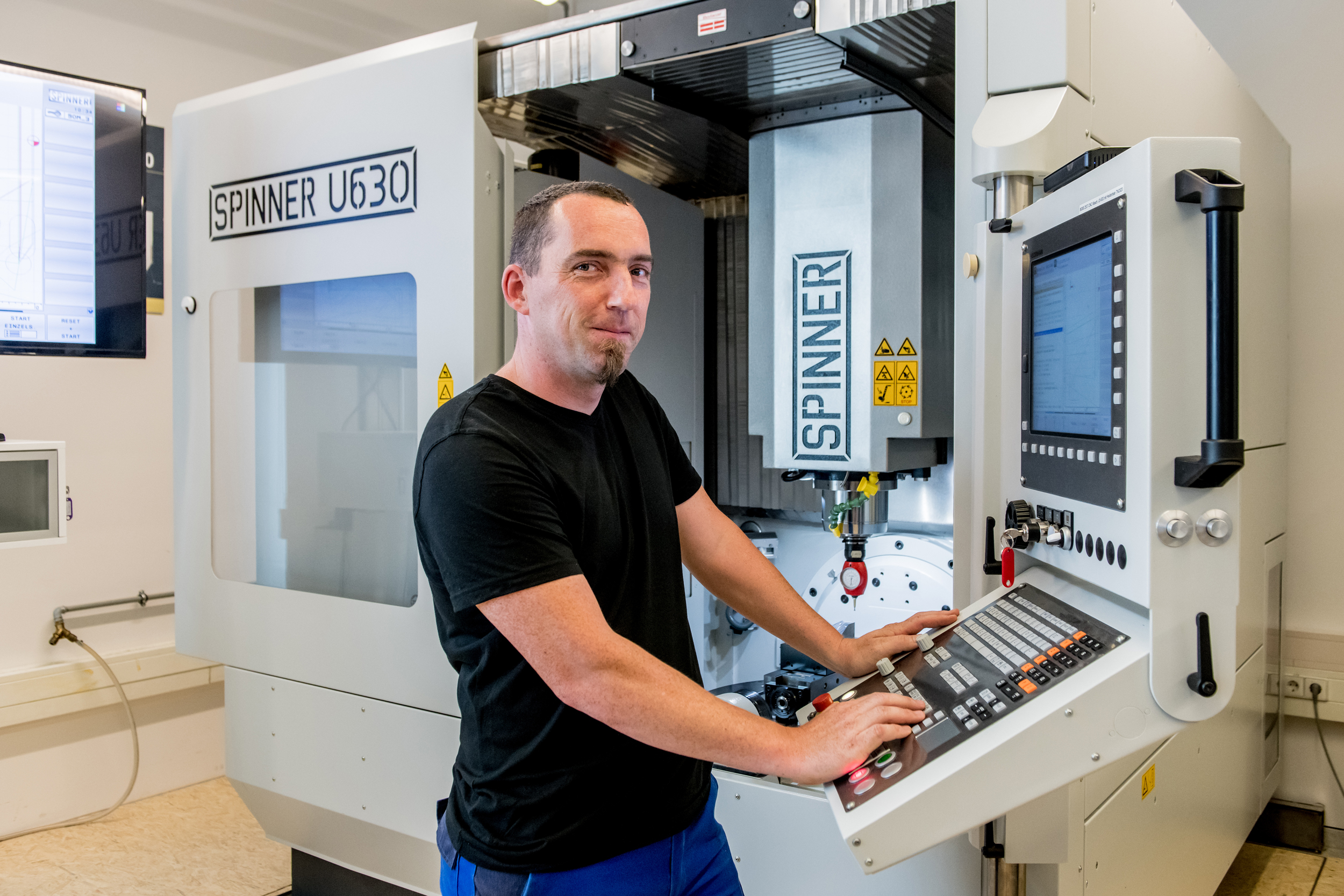 Ein junger Mann steht lächelnd vor einer CNC-Maschine
